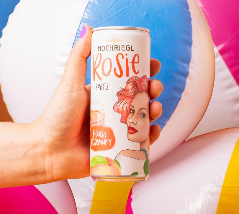 Dame hält eine Dose Rose vor aufgeblasenen Wasserbällen
